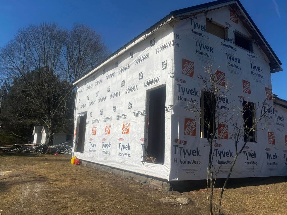 House under construction, wrapped in Tyvek, with empty door and window frames. Sunny day.