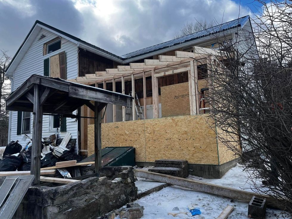 House under construction with exposed wooden framing and OSB siding. Snow on the ground.