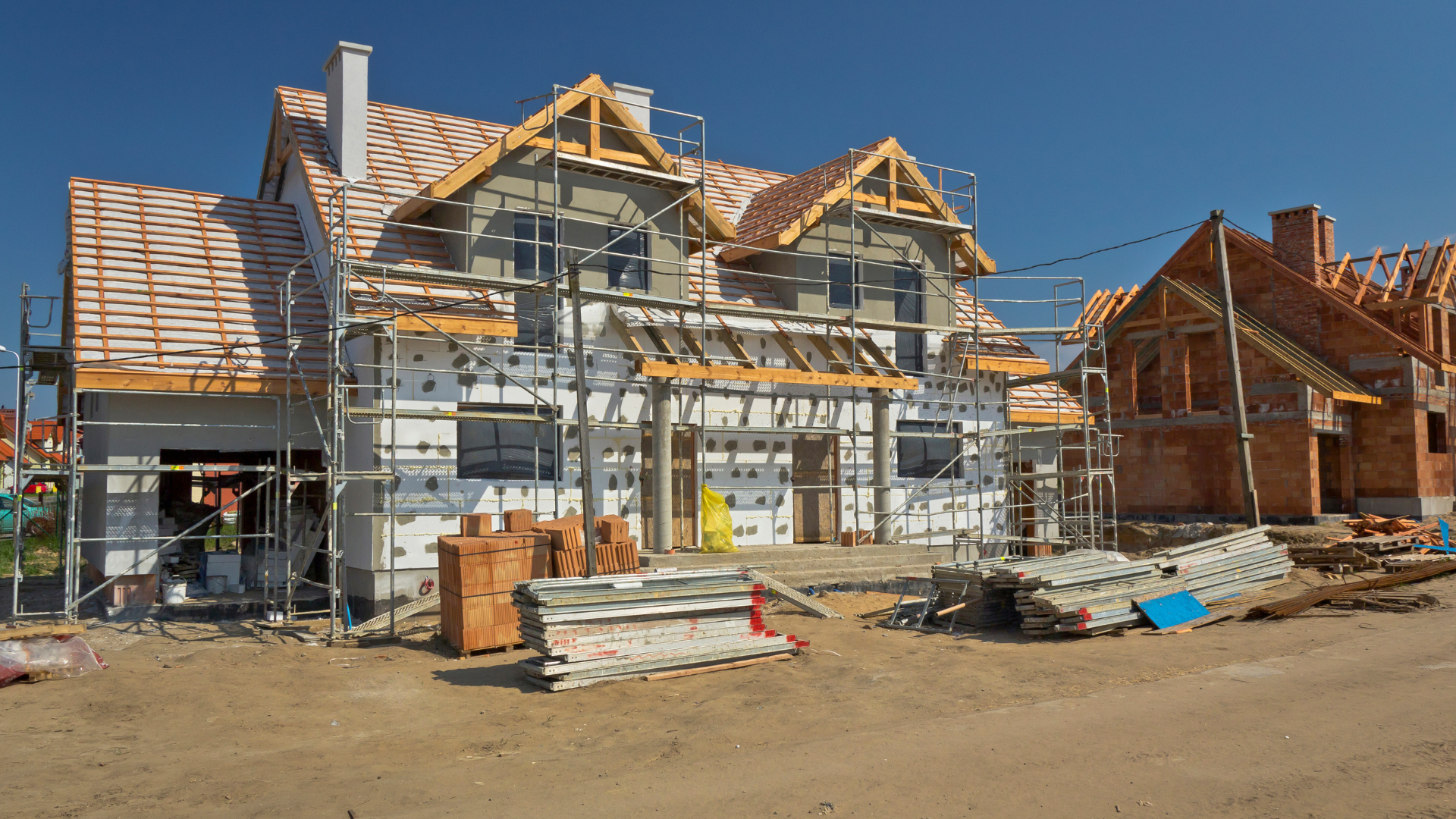 Houses under construction, scaffolding, exposed framing, brick, clear blue sky.