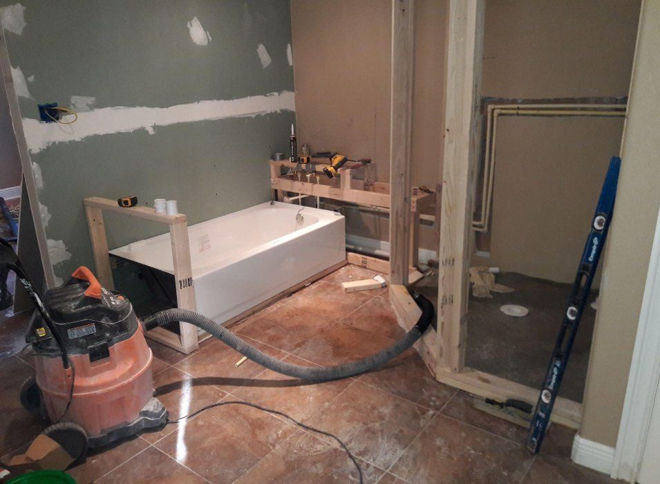 Bathroom renovation in progress; tub, framing, and vacuum are visible. Drywall and plumbing partially installed.