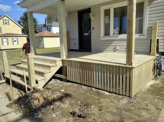 New wooden porch under construction with steps, siding, and railings in front of a house.