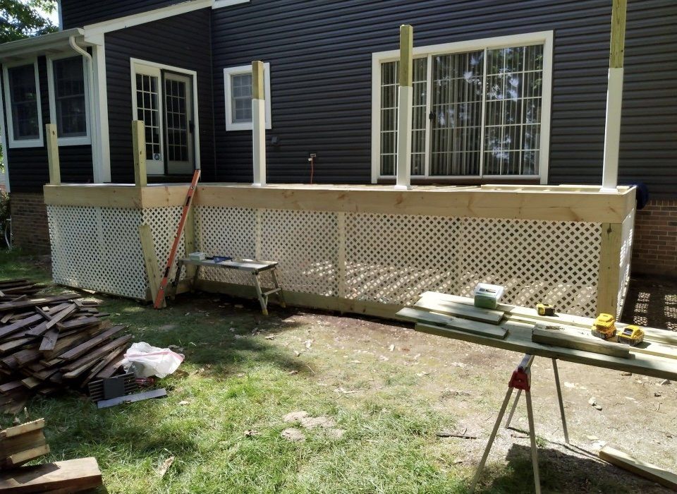 Deck construction in progress; white lattice skirting, lumber, tools, and black house.
