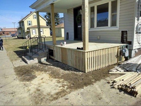 Newly built wooden porch with vertical siding, next to a sidewalk and house.