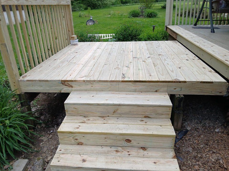 Wooden deck with three steps leading down to the ground in a grassy outdoor setting.