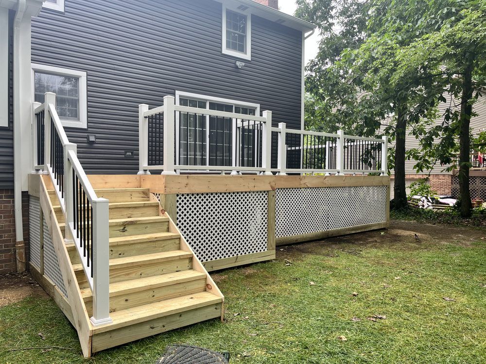 Wooden deck with white railing and stairs against a dark house.