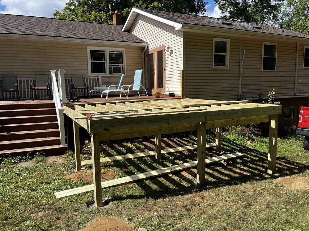 Deck under construction next to a tan house with green grass, showing the frame.