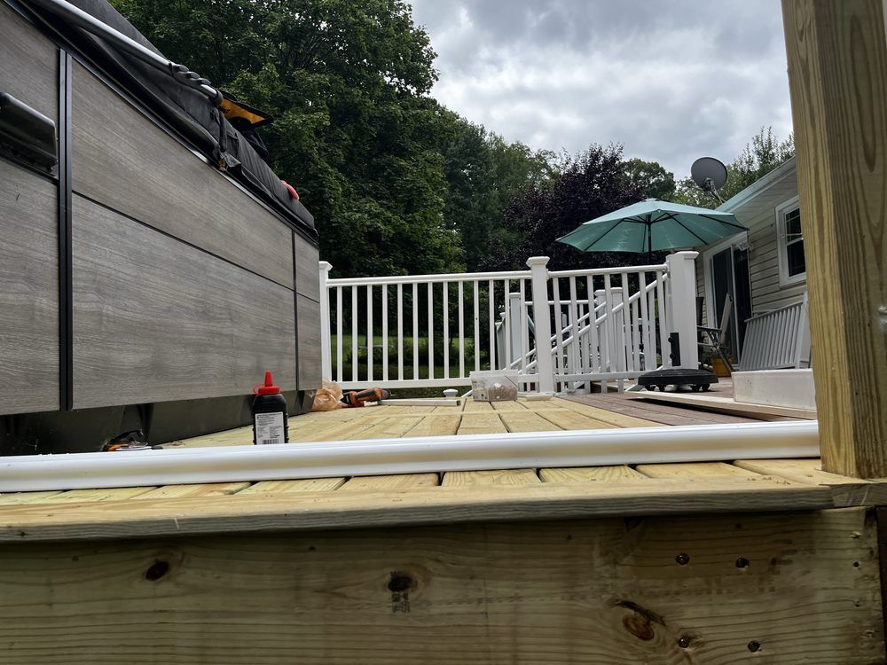 Deck with hot tub and white railing; lumber and construction materials visible.