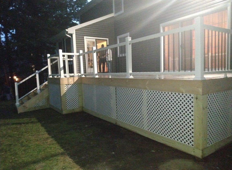 A newly built wooden deck with white railing and lattice skirting, attached to a house.