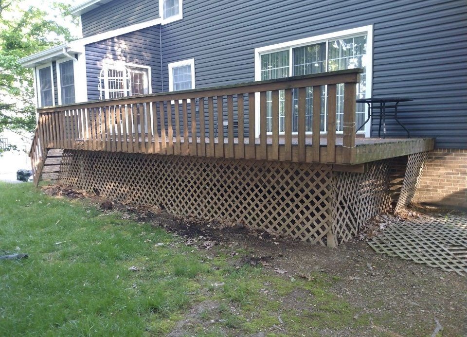 A weathered wooden deck attached to a dark-sided house, with lattice skirting and a grassy yard.