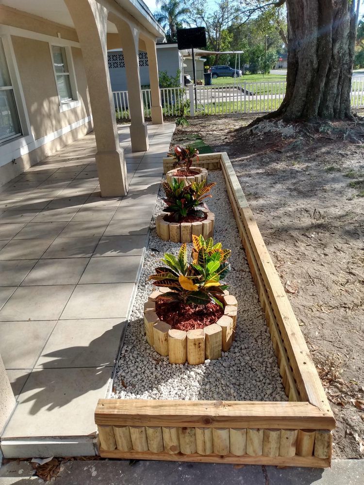 A row of decorative planters with plants and mulch along a building's walkway.