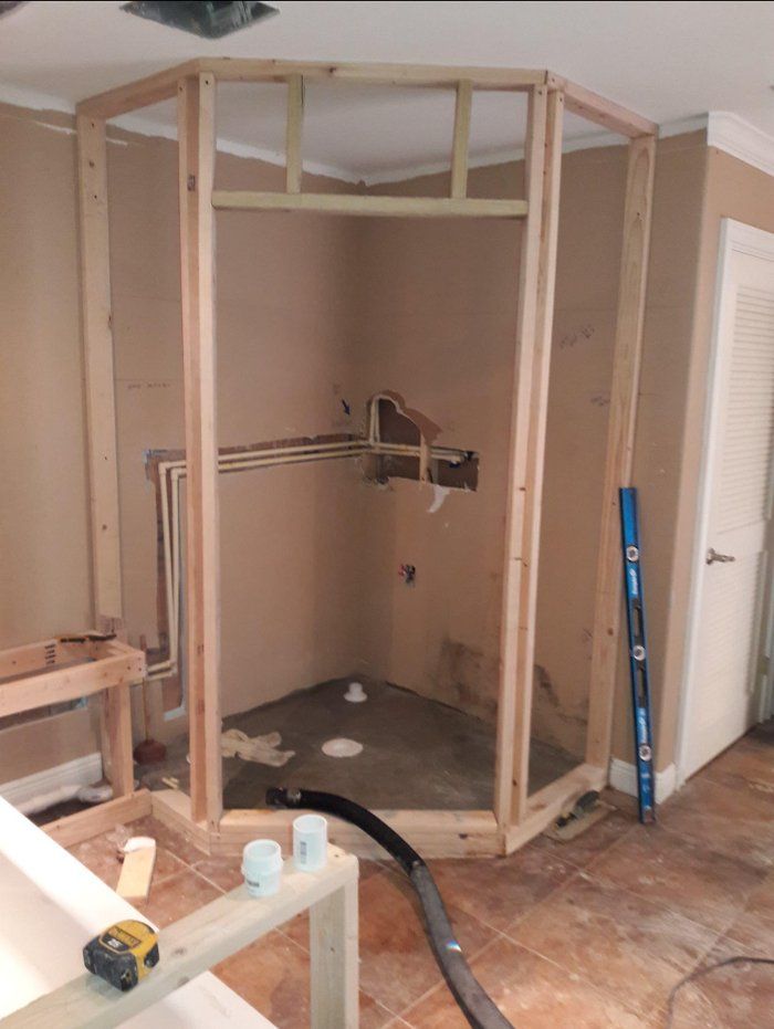 Shower framing under construction in a room, with exposed pipes and a level leaning against a wall.