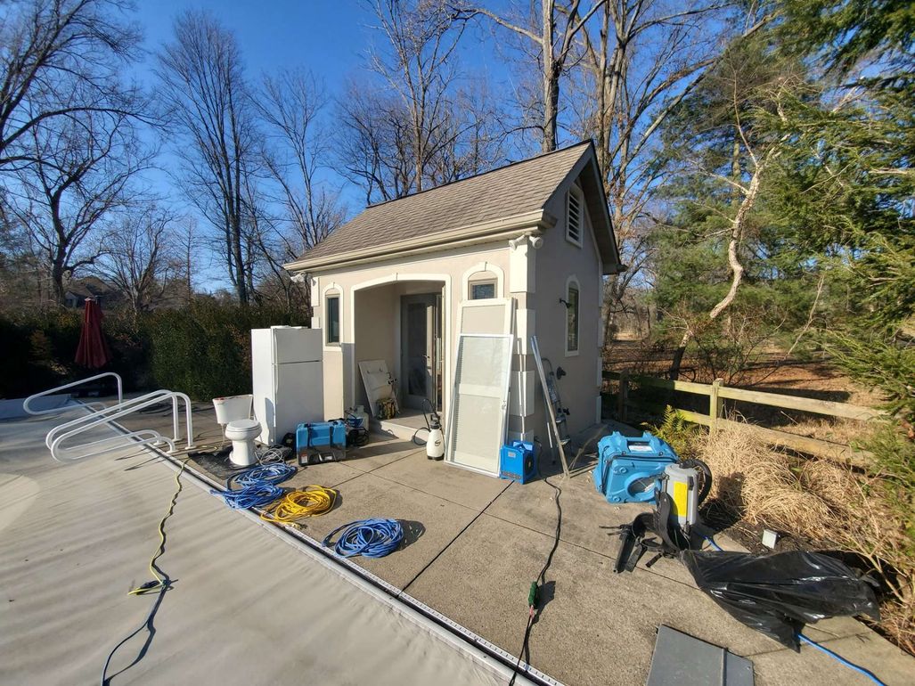 A small pool house with equipment and maintenance supplies scattered on the concrete patio beside a covered pool.