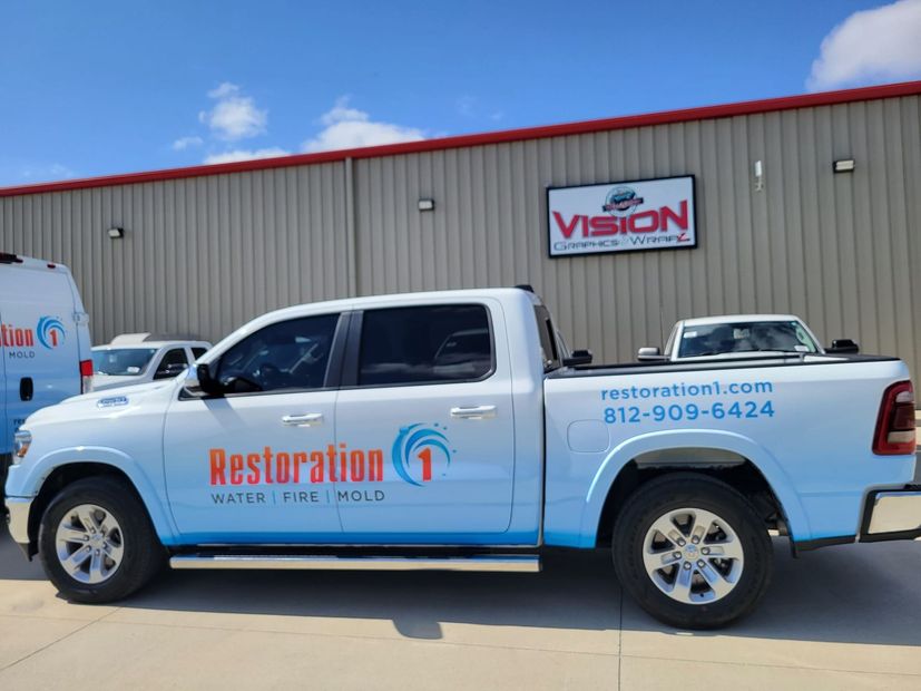 A white Restoration 1 pickup truck parked in front of a tan industrial building with a Vision logo sign.