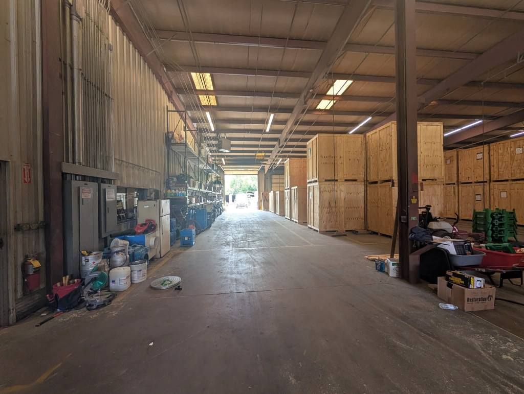 A wide, central aisle in a warehouse with stacked wooden crates on the right and storage items along the left wall.