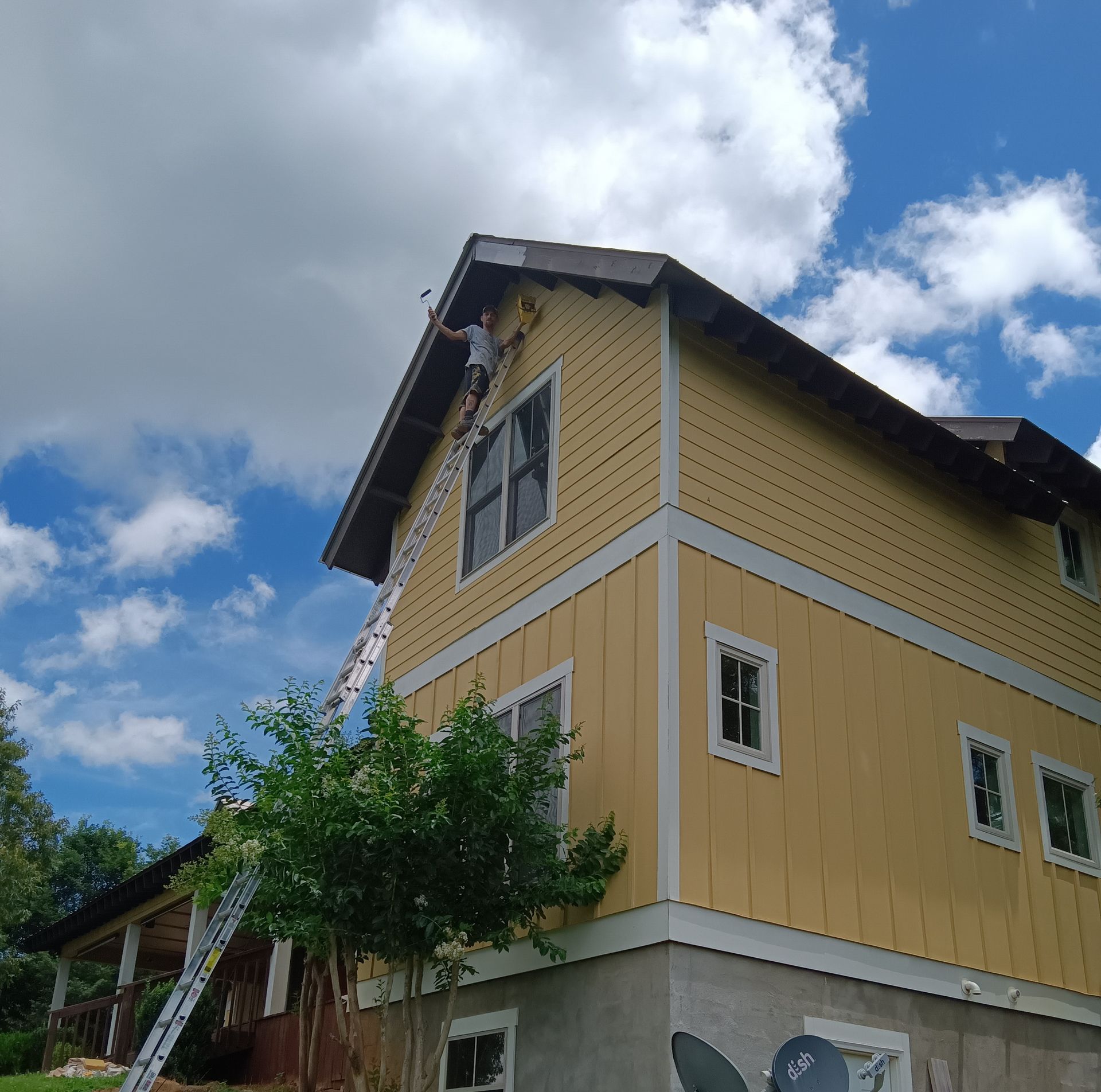 A man on a ladder paints the side of a house