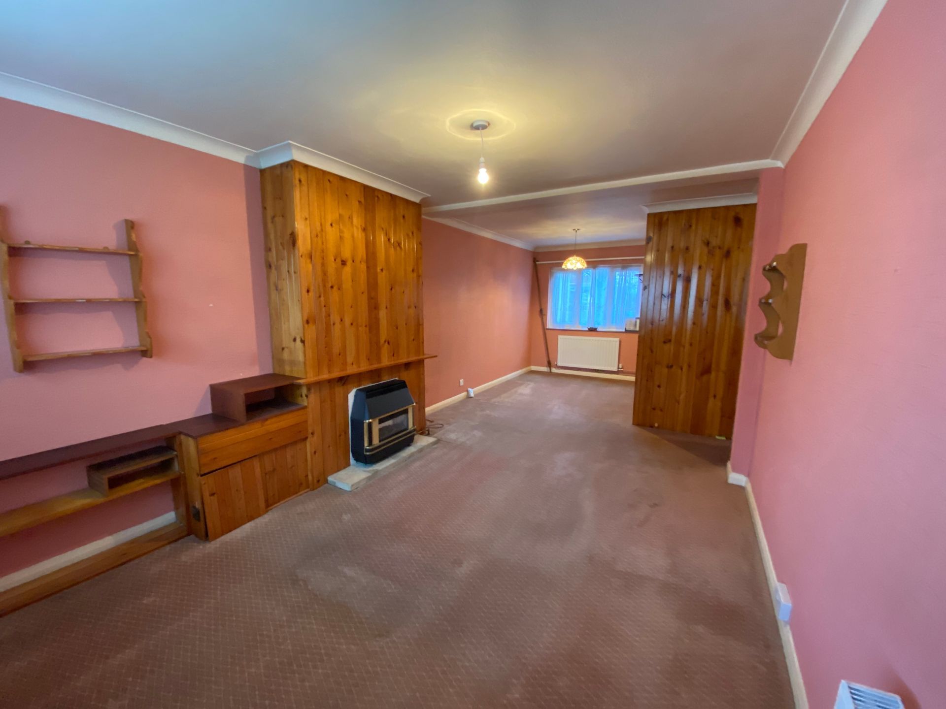 An empty living room with pink walls and a fireplace.