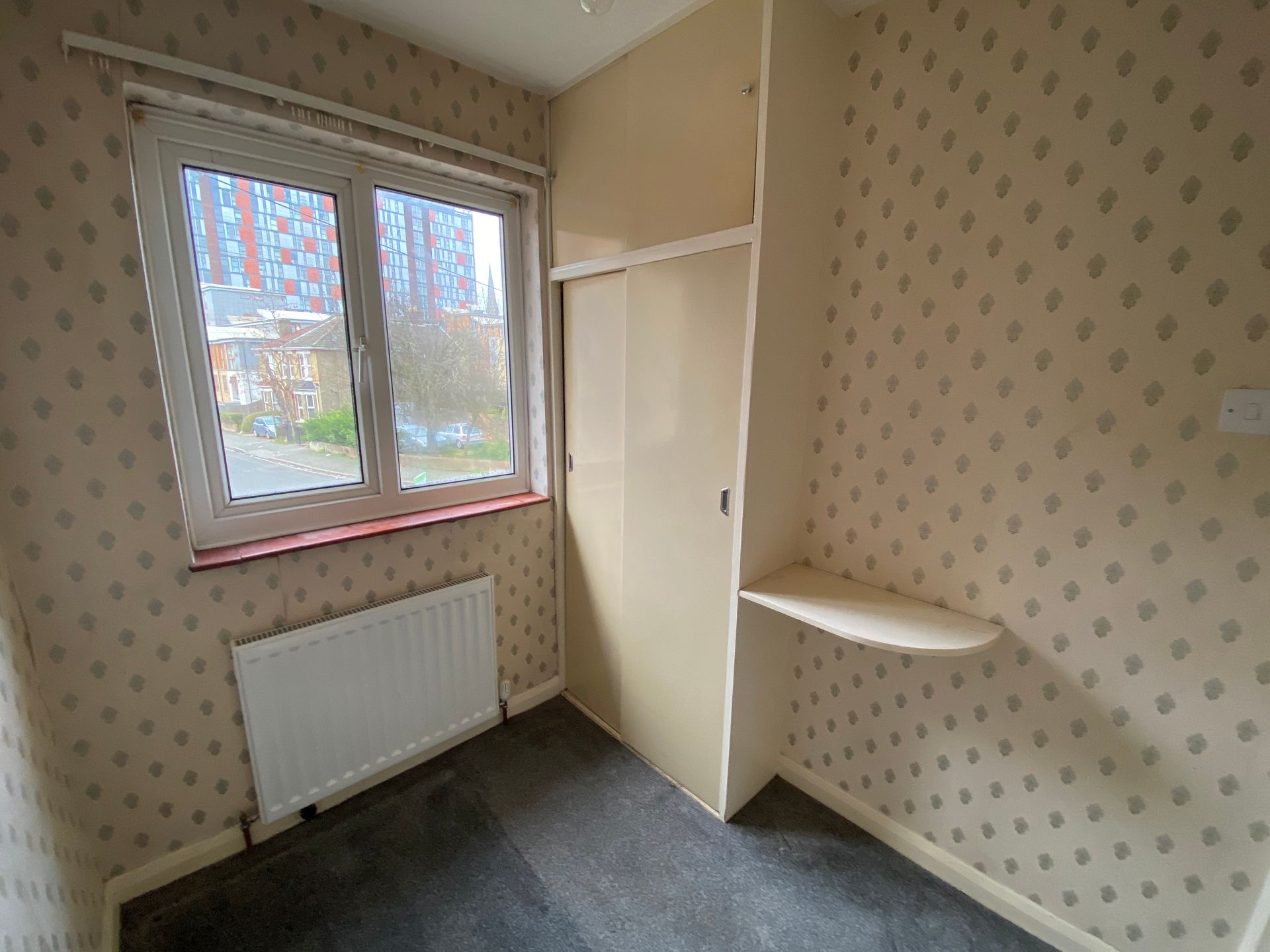 An empty bedroom with a window and a shelf.