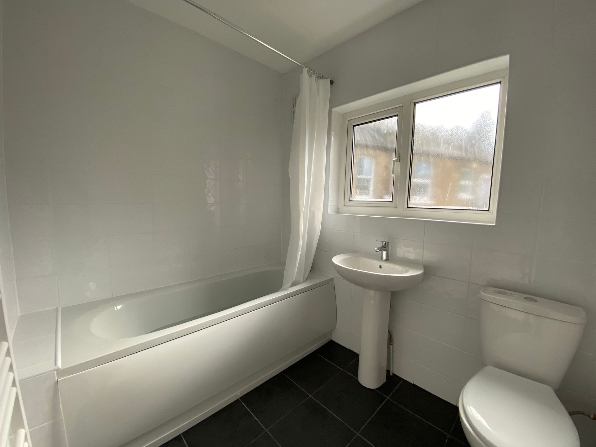 A bathroom with a tub , sink , toilet and window.