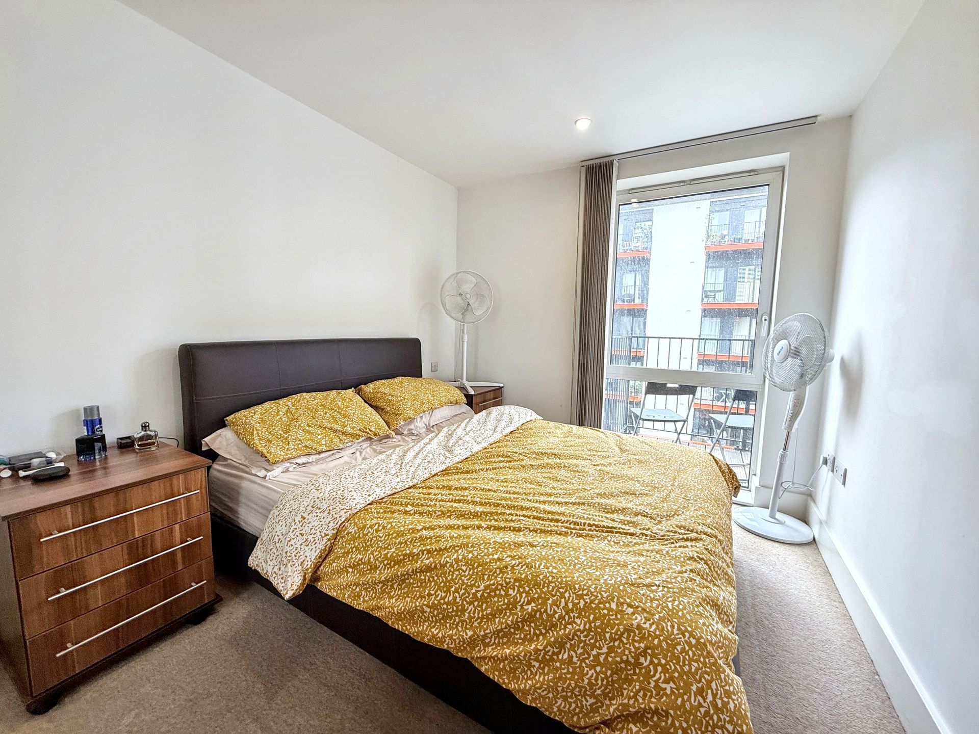 A bedroom with a large bed , dresser , nightstand and fan.