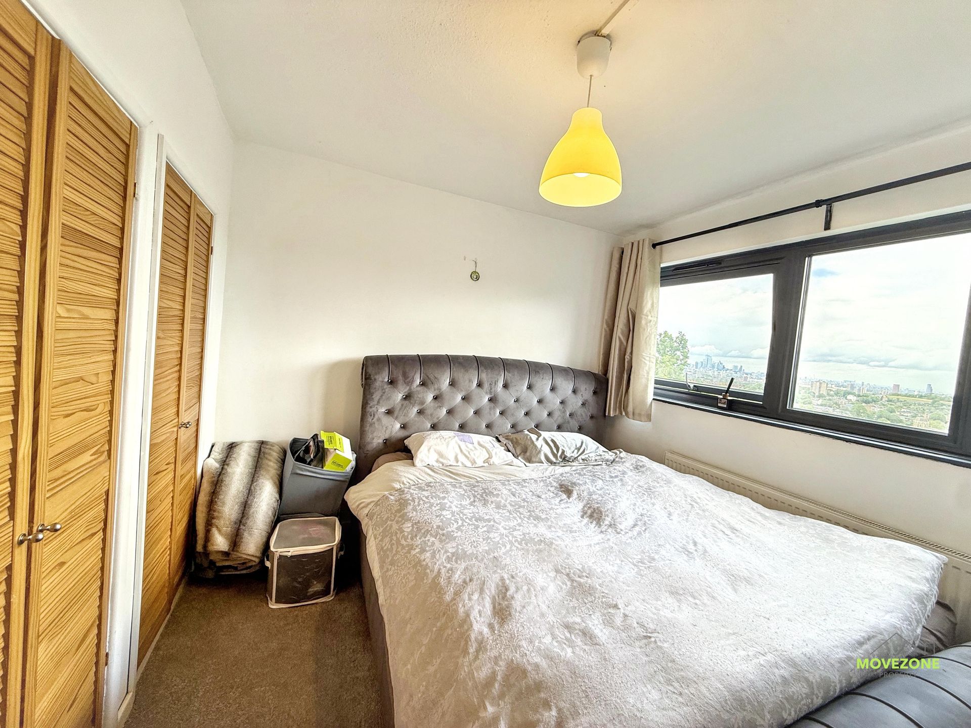 Bright bedroom with a bed, wooden closet, and large window overlooking a view.