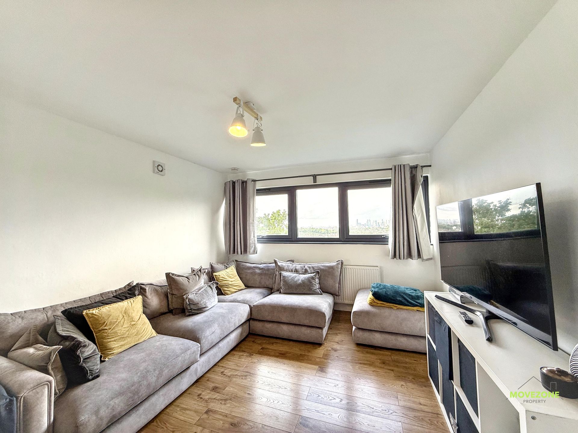 Bright living room with gray sectional, TV, wooden floor, and large window with curtains