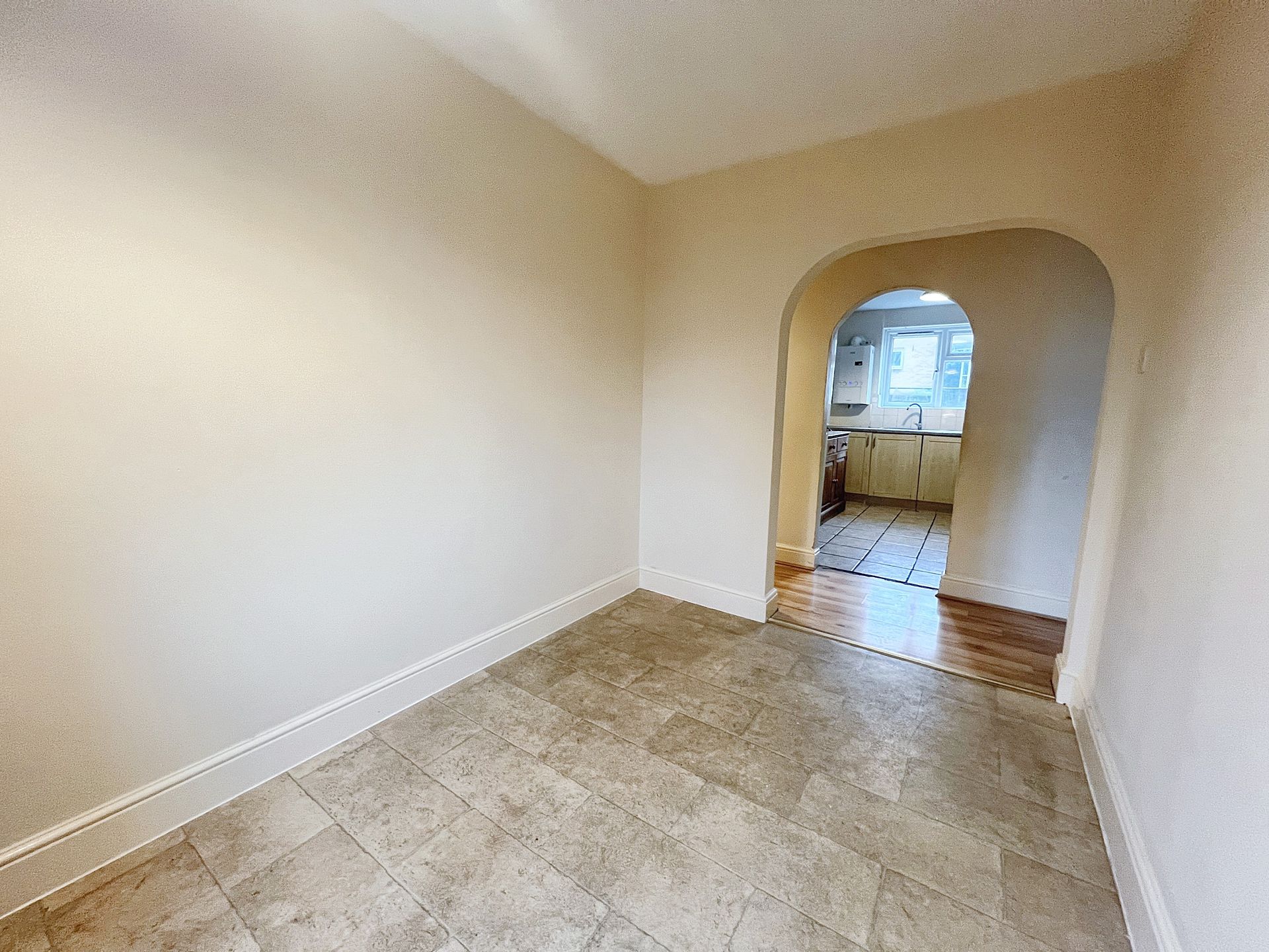 An empty room with a tiled floor and a doorway leading to a kitchen.