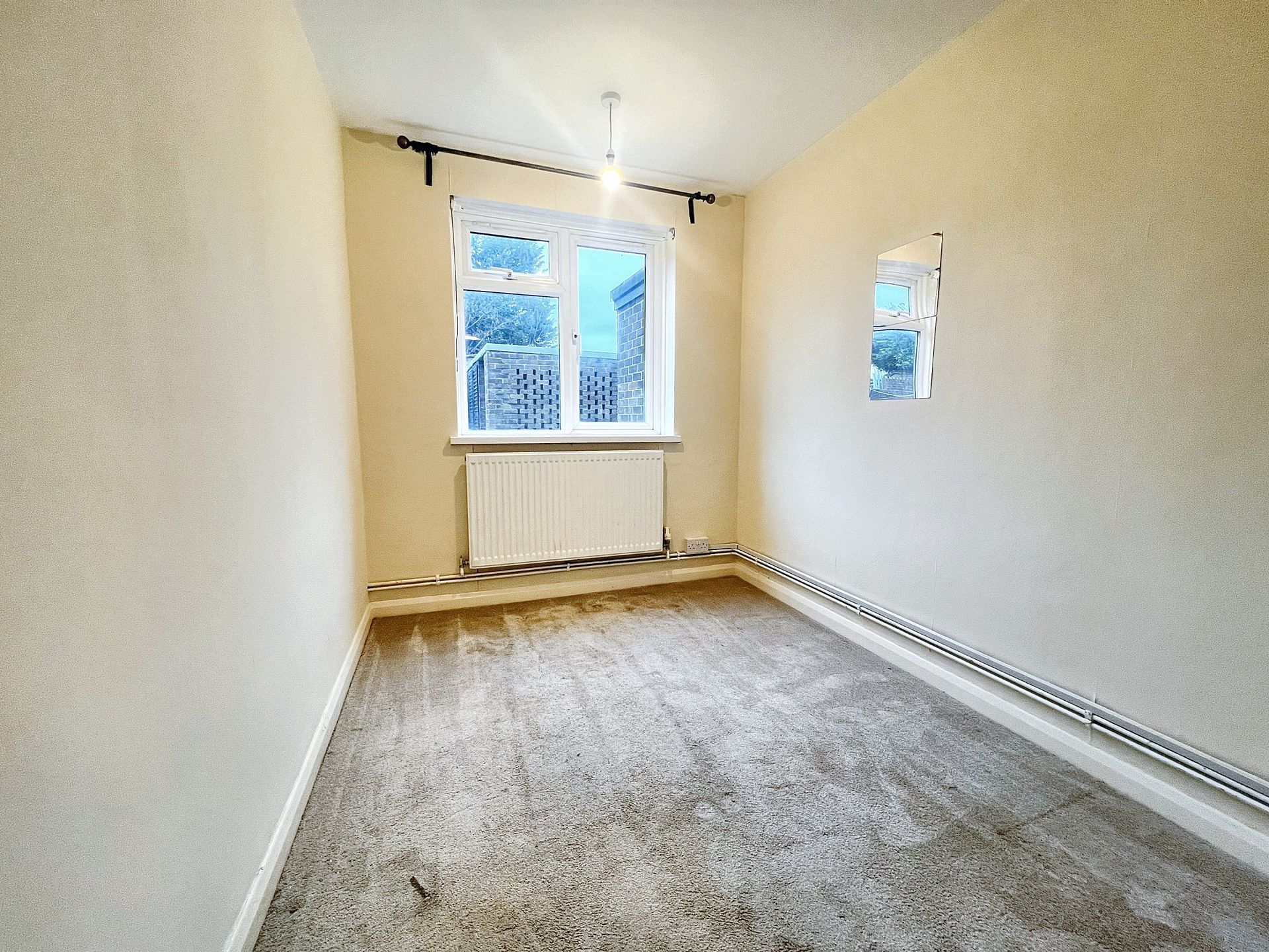 An empty bedroom with a radiator and two windows.