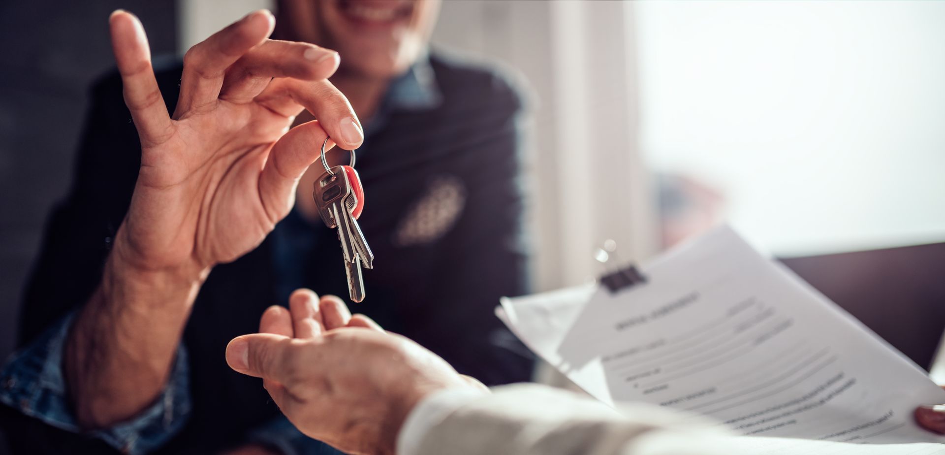 A person hands keys to another individual while holding a document, representing a property or business transaction.