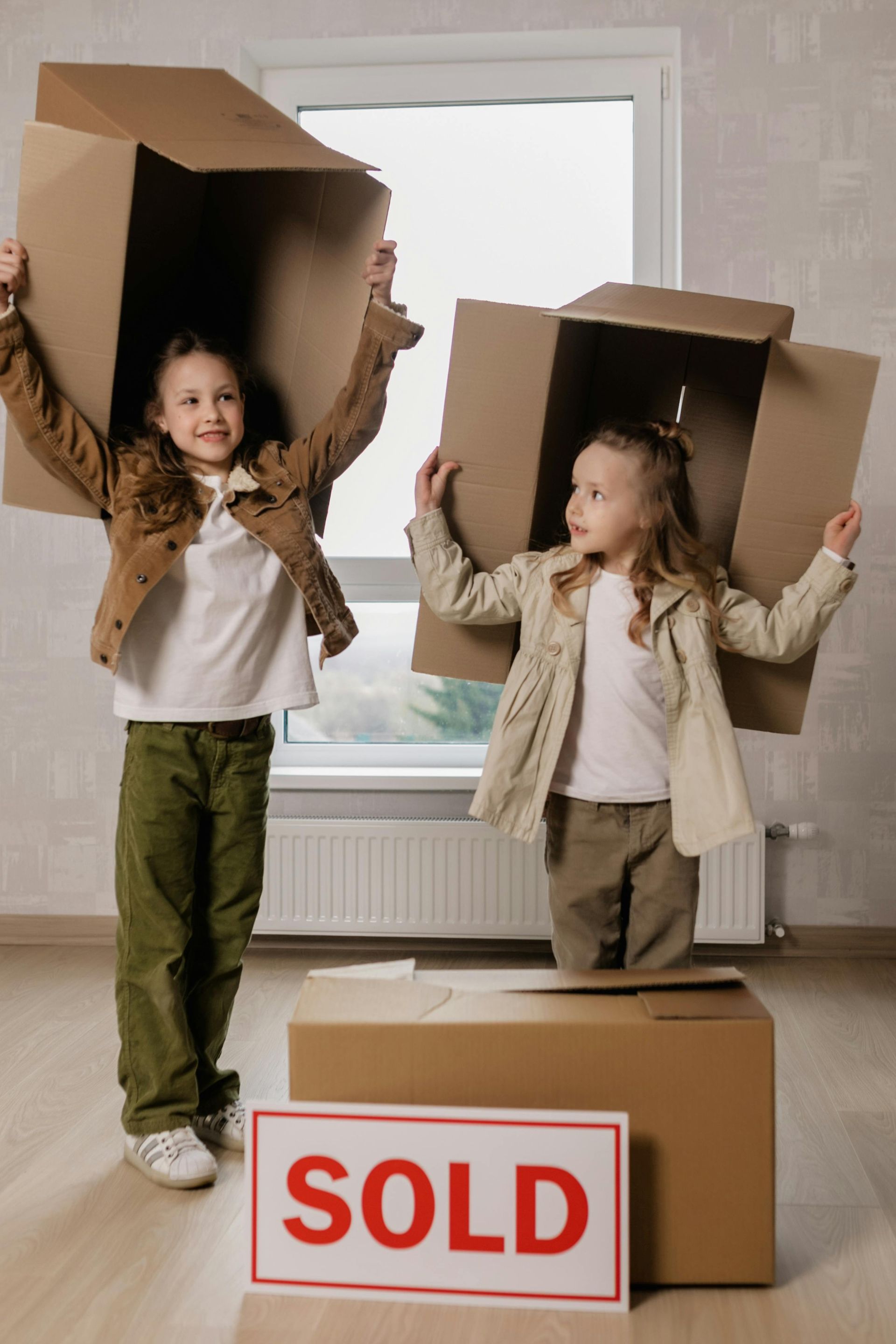 Two children are playing with cardboard boxes and a sold sign.
