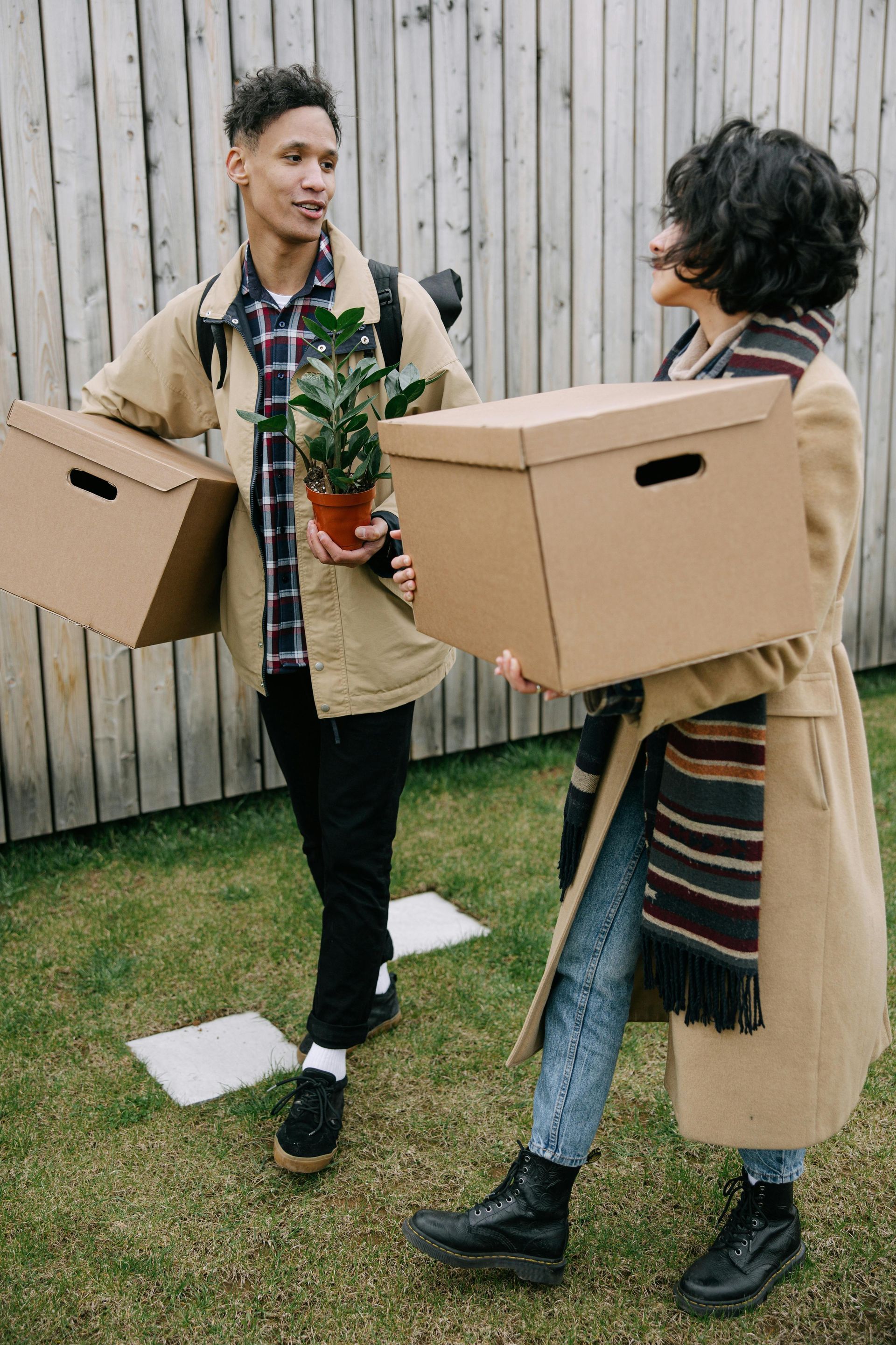 A man and a woman are carrying cardboard boxes and a potted plant.