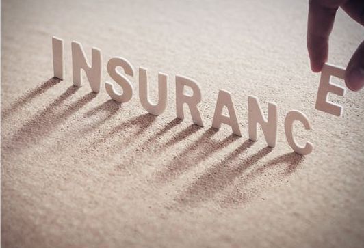Wooden letters spelling “INSURANCE” casting long shadows on a beige surface