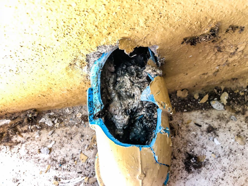 Damaged Blue Pipe Embedded in a Yellow Wall, Filled With Debris — Gibson Plumbing & Roofing Pty Ltd in Biloela, QLD