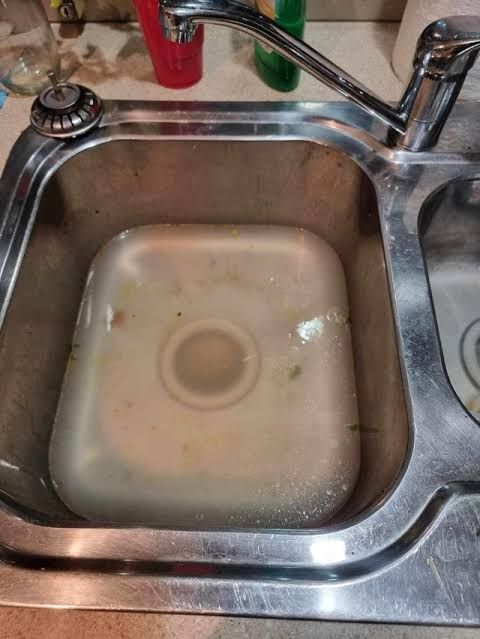 Dirty Water Pooling In A Stainless Steel Kitchen Sink With A Drain At Center — Gibson Plumbing & Roofing Pty Ltd in Boyne Island, QLD