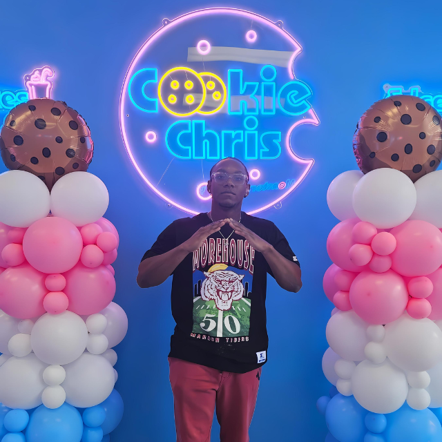A man stands in front of a sign that says cookie chris