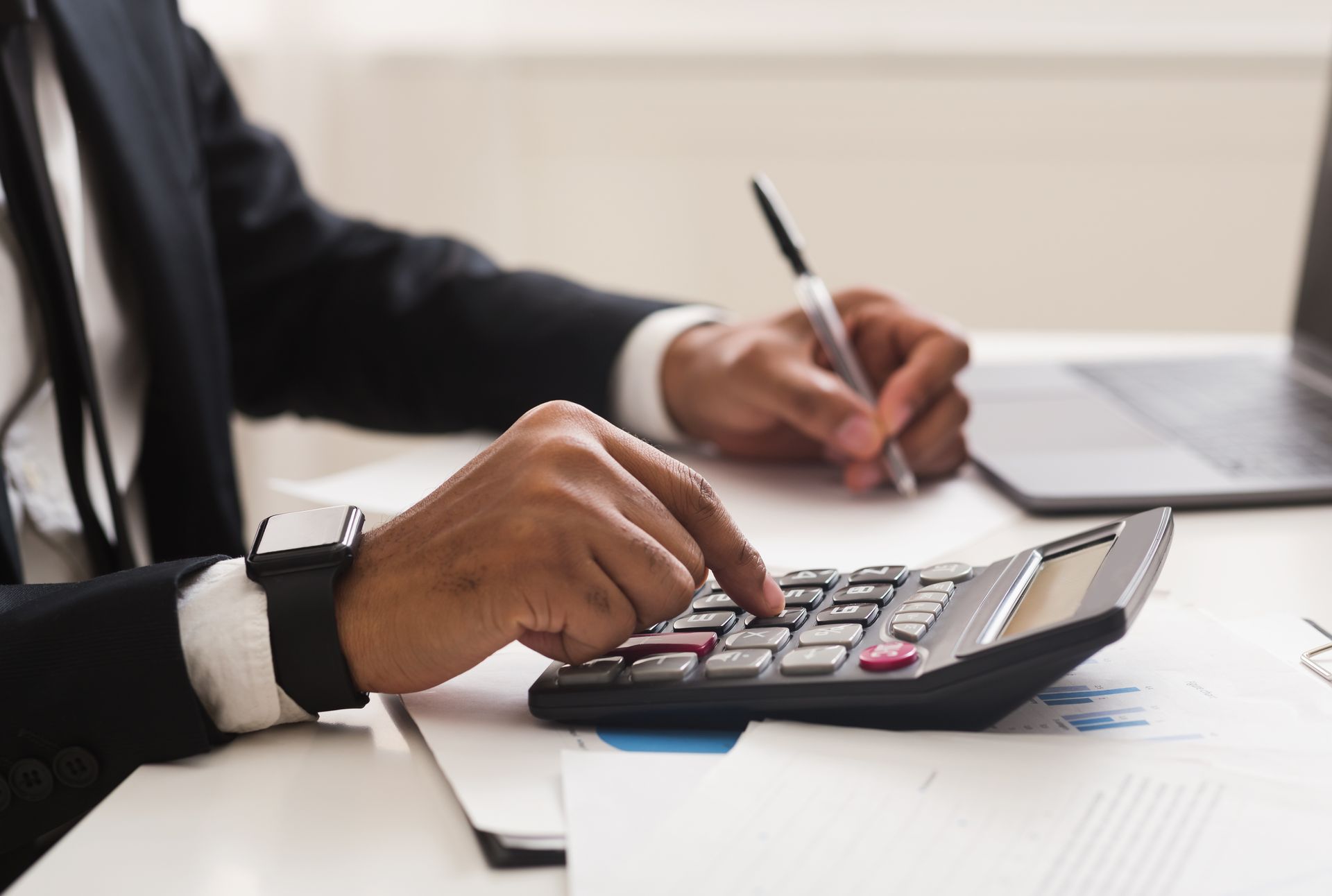 Person in suit using a calculator and writing on paper at a desk.