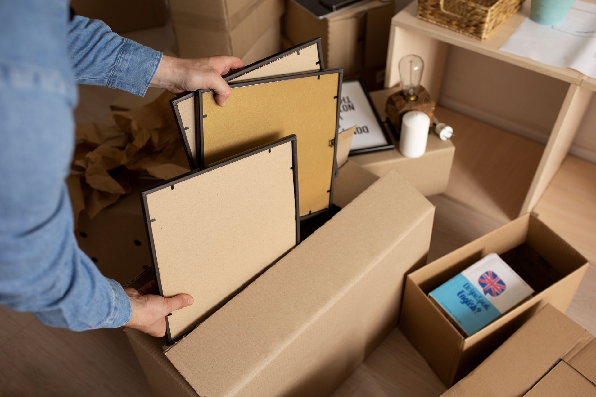 A person is holding a picture frame in a cardboard box.