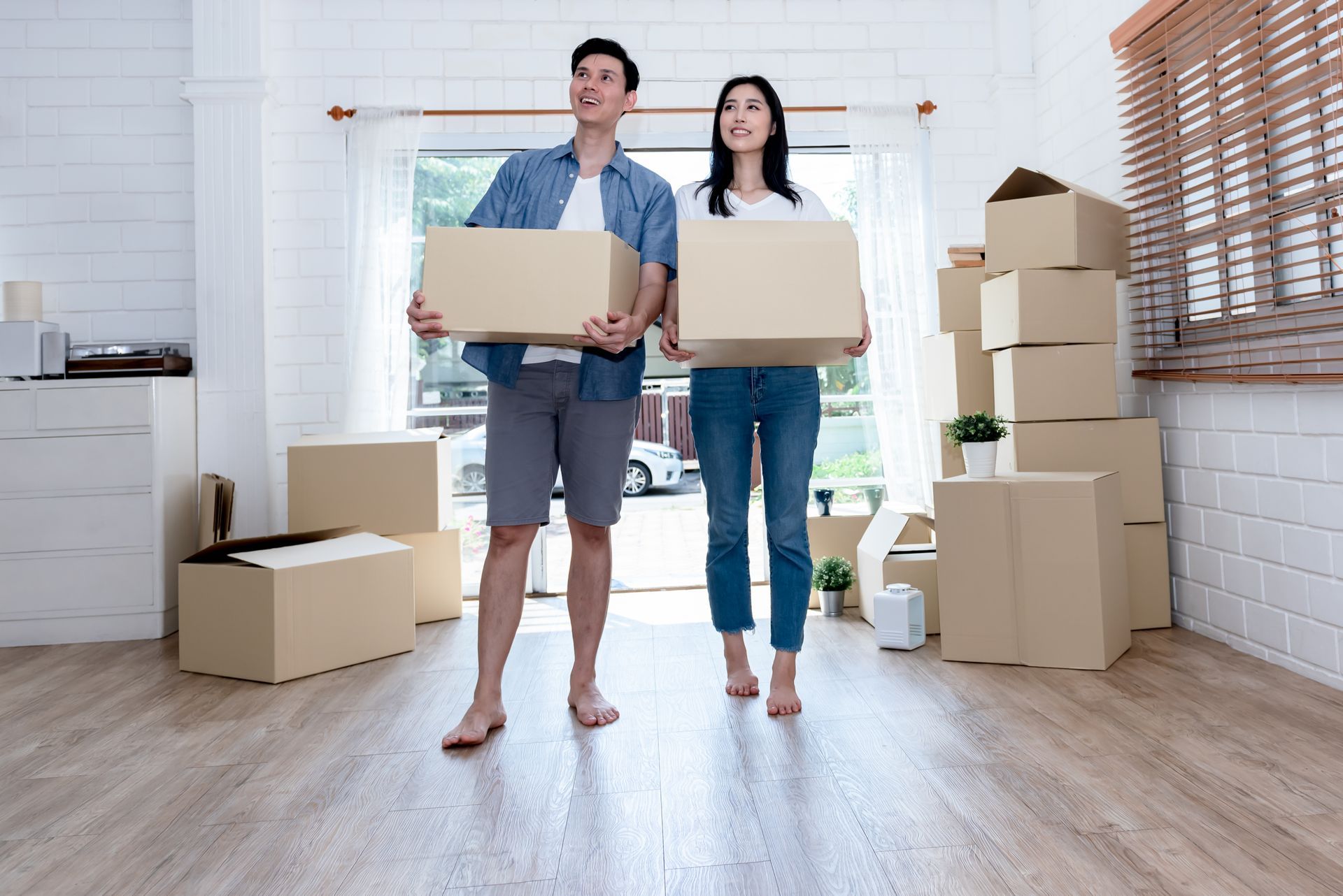 A man and a woman are holding cardboard boxes in a living room.