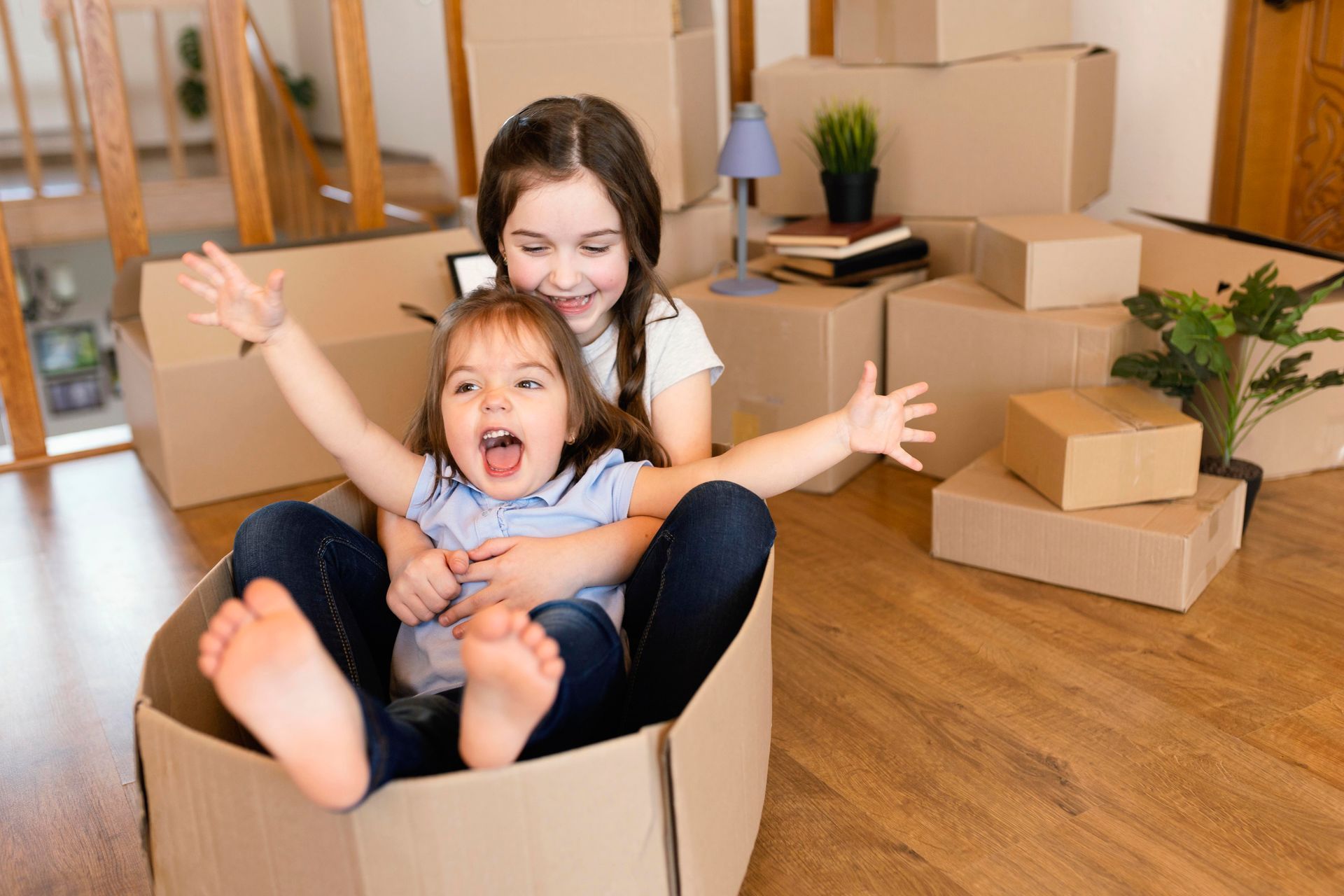 Two little girls are sitting in a cardboard box.