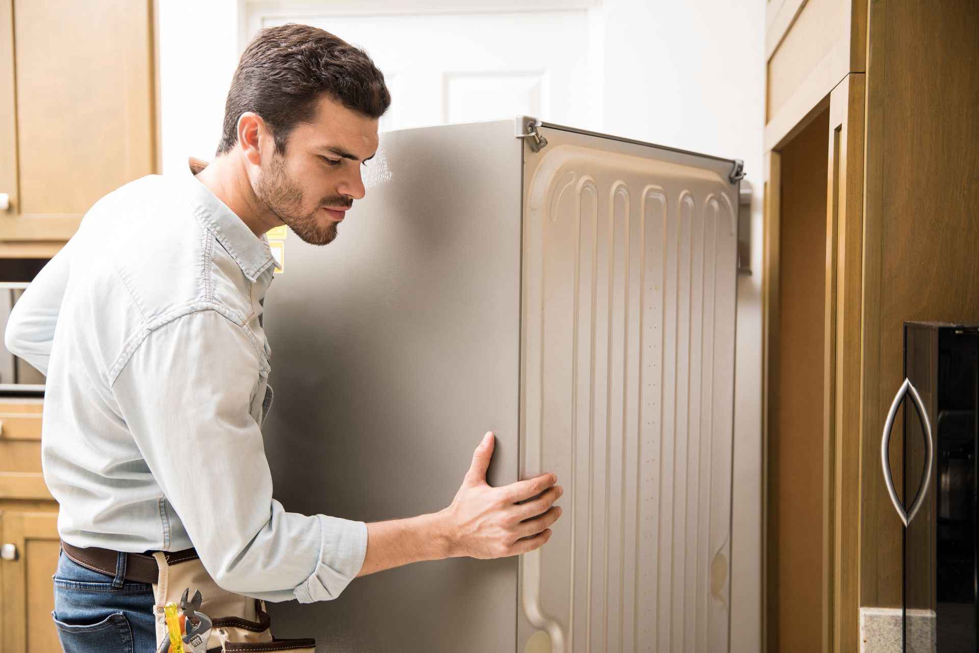 A man is fixing a refrigerator in a kitchen.