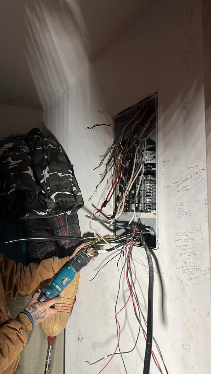 A man is working on an electrical box with a drill.