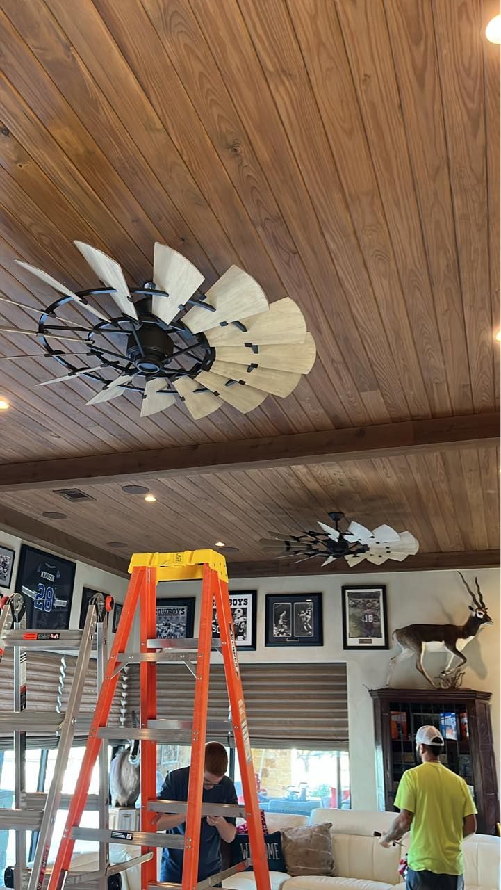 A group of people are working on a ceiling fan in a living room.