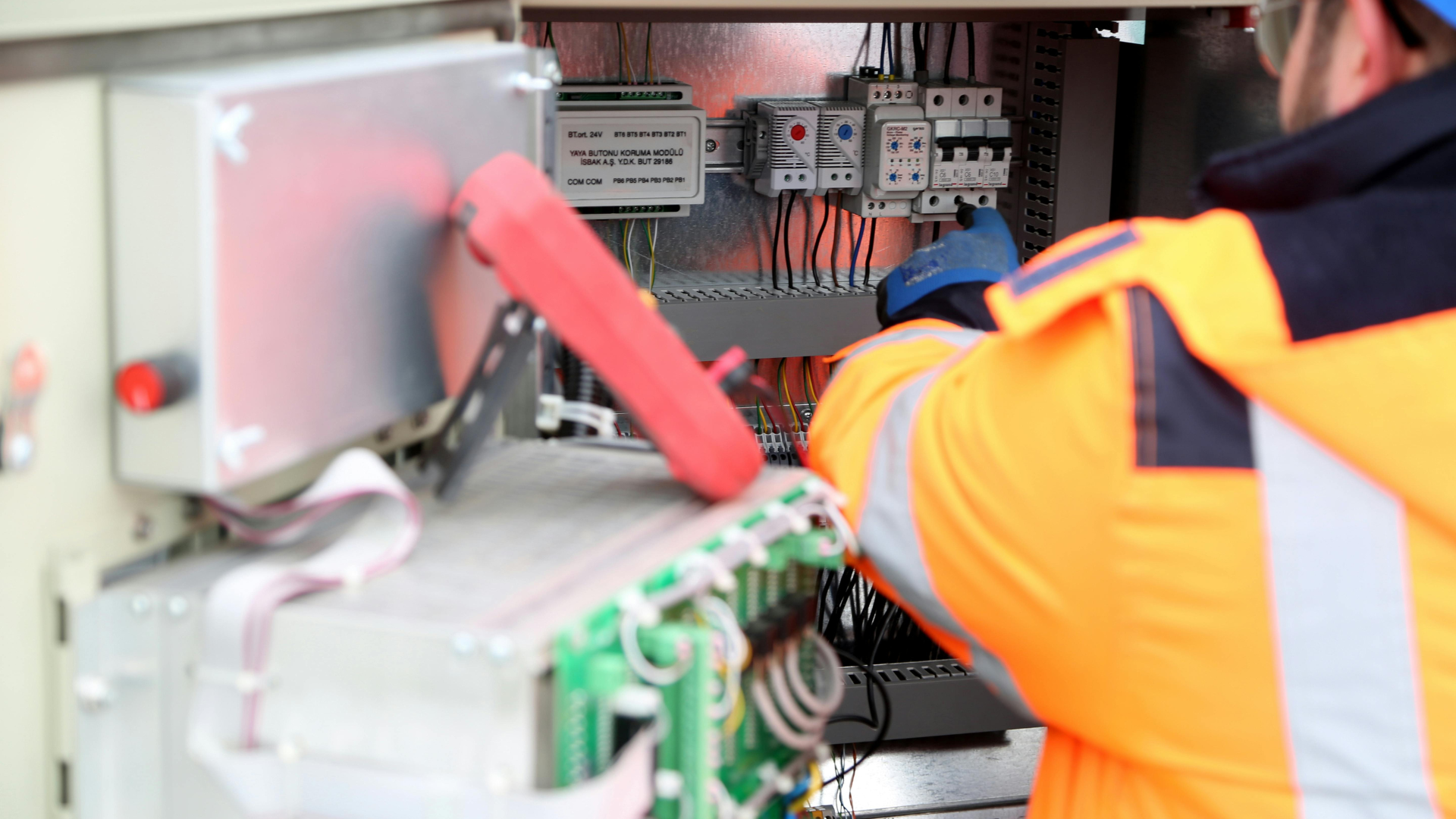A man in an orange jacket is working on a electrical box.