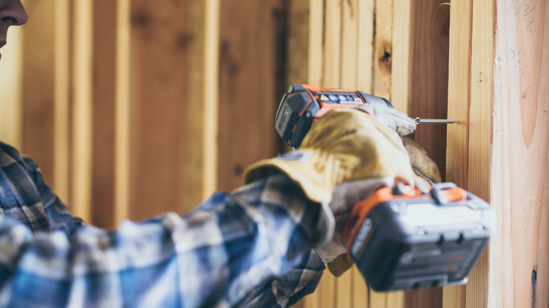A man is using a drill to drill a hole in a wooden wall.