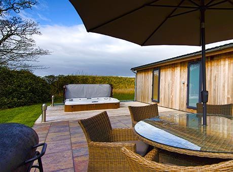 Un patio avec une table et des chaises et un parasol avec un bain à remous en arrière-plan.