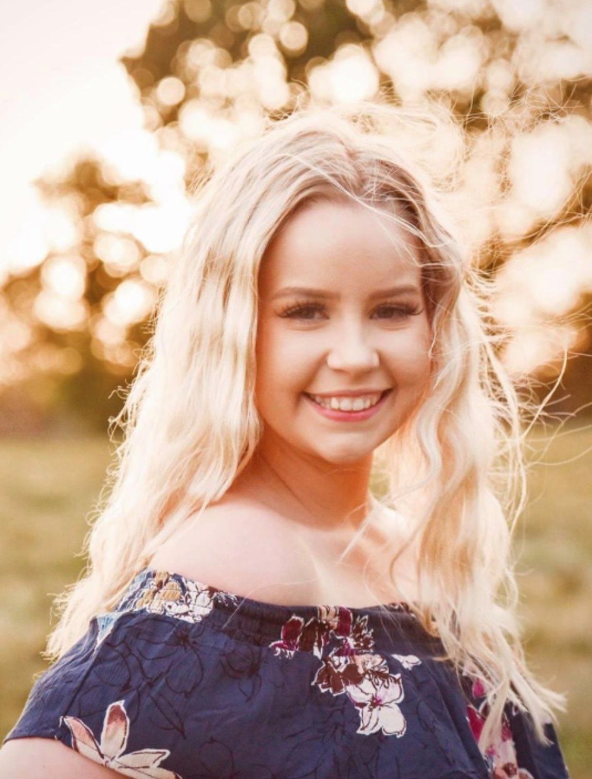 A woman in a blue floral off the shoulder top is smiling for the camera.