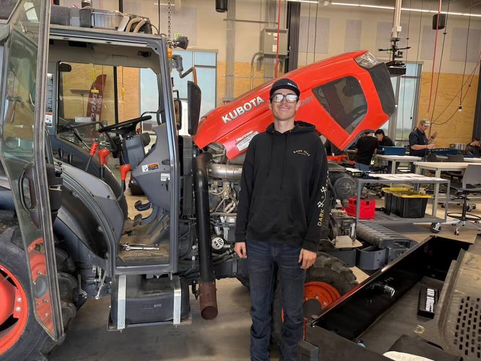 A man is standing in front of a kubota tractor in a garage.