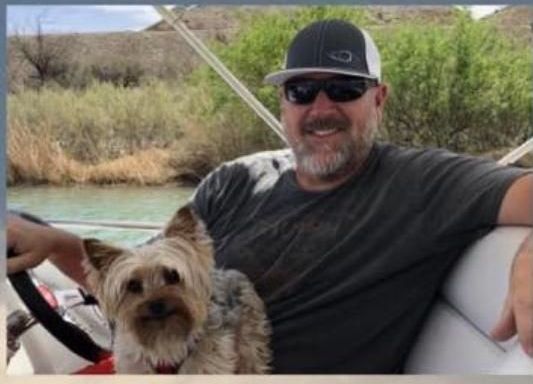 A man is sitting on a boat with a small dog
