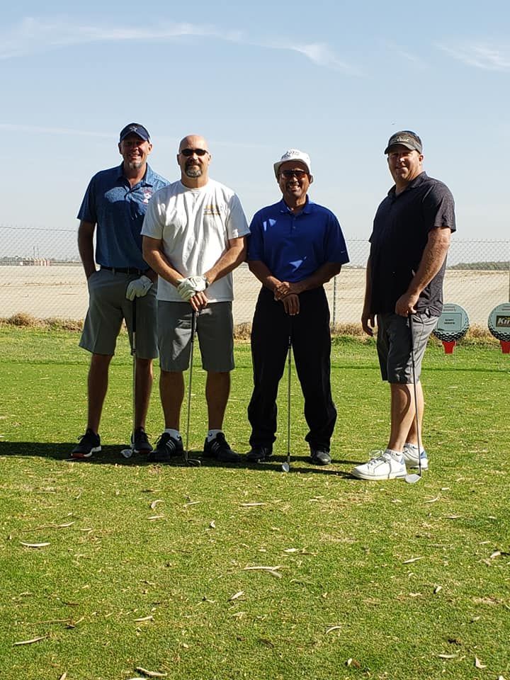 Four men standing on a golf course holding golf clubs