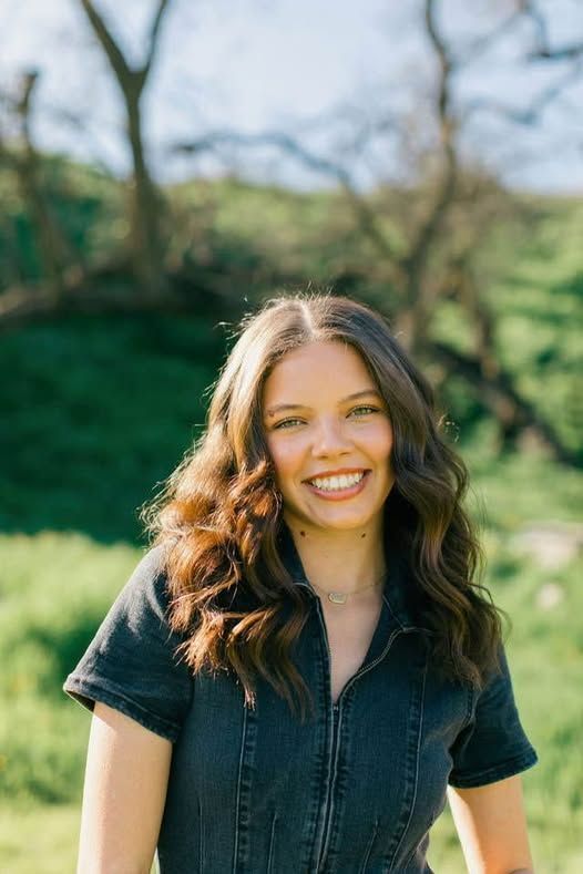 A woman in a black dress is smiling in a field.