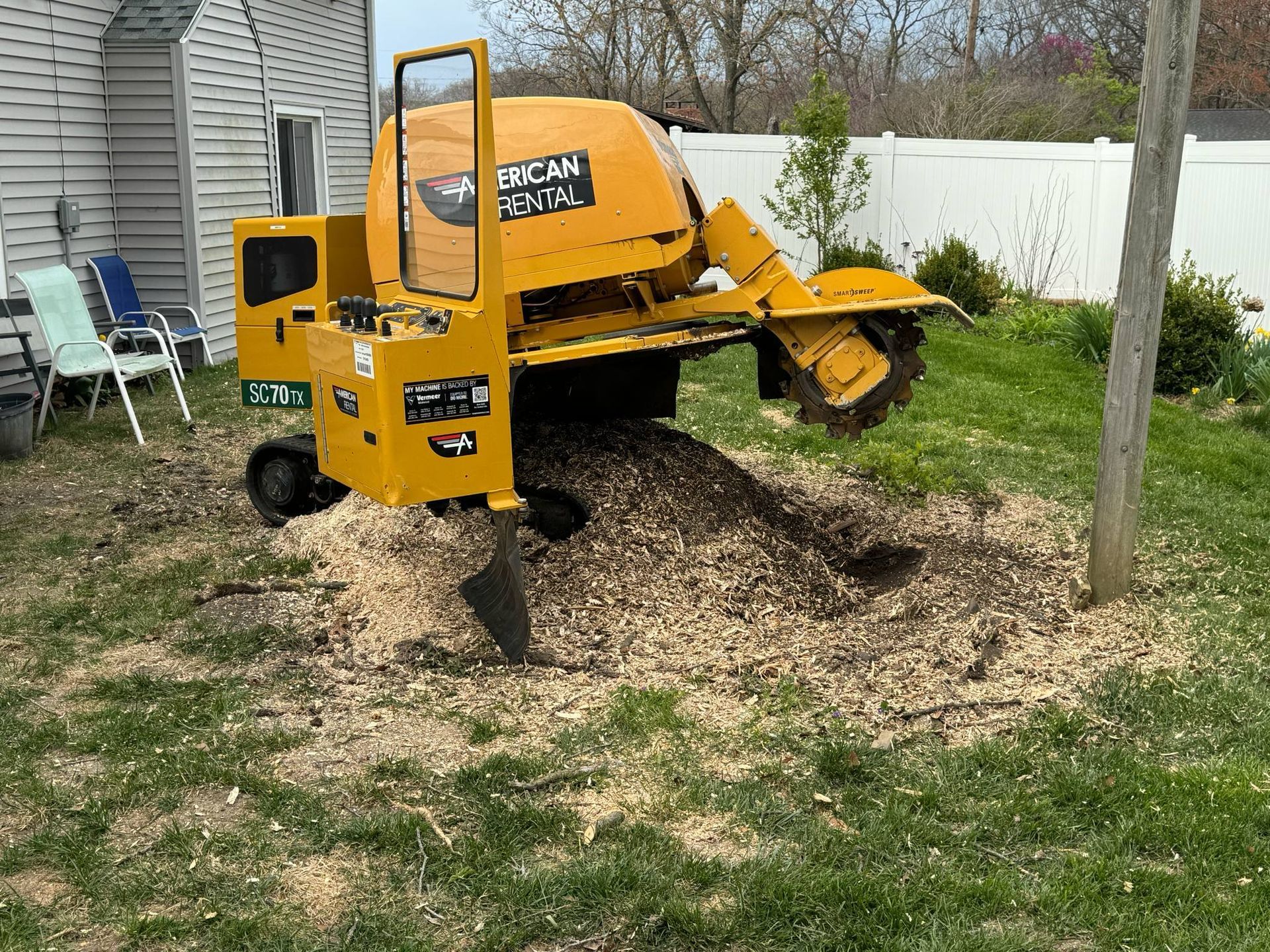 A yellow stump grinder is sitting in the grass in front of a house.